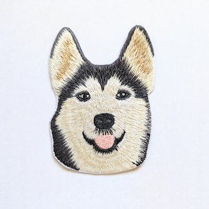 Puede incluir: Parche bordado con la cara de un perro husky. El perro tiene pelo blanco y negro con orejas marrones y la lengua rosa fuera.