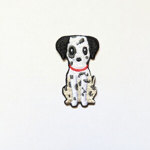 May include: An embroidered patch of a Dalmatian dog, featuring black and white spots and a red collar. The dog is depicted sitting with its front paws together and its back legs slightly apart.