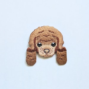 May include: Embroidered patch of a brown poodle with a cute expression. The patch is ideal for adding a touch of whimsy to clothing, bags, or other accessories.