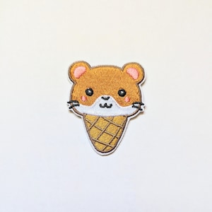 May include: A brown and white embroidered patch of a cartoon hamster wearing an ice cream cone.