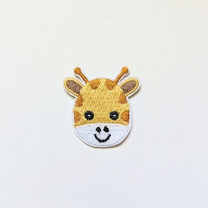 May include: A yellow and brown embroidered patch of a giraffe's face with a white background and a smiling expression.