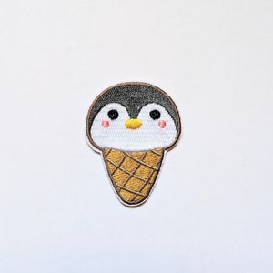 May include: Embroidered iron-on patch of a penguin wearing an ice cream cone. The penguin is white with a black head and beak, and the ice cream cone is brown and yellow.