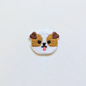 May include: White embroidered patch of a dog's face with brown ears, black eyes, and a pink tongue sticking out.