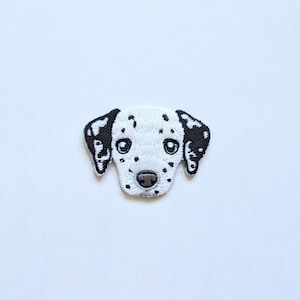 Puede incluir: Parche bordado de la cara de un dálmata con manchas negras sobre fondo blanco.
