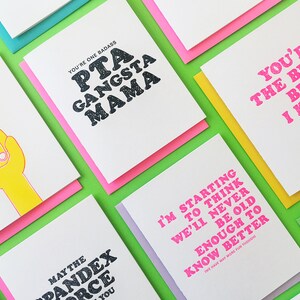 May include: A collection of greeting cards with various humorous and sassy messages printed in bold, colorful fonts. The cards are displayed on a green background.