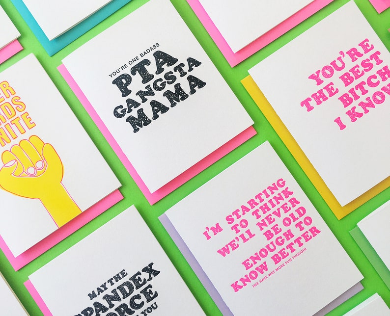 May include: A collection of greeting cards with various humorous and sassy messages printed in bold, colorful fonts. The cards are displayed on a green background.