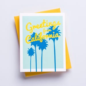 May include: A greeting card with a blue sky background and yellow text that reads "Greetings from California". The text is surrounded by blue palm trees.