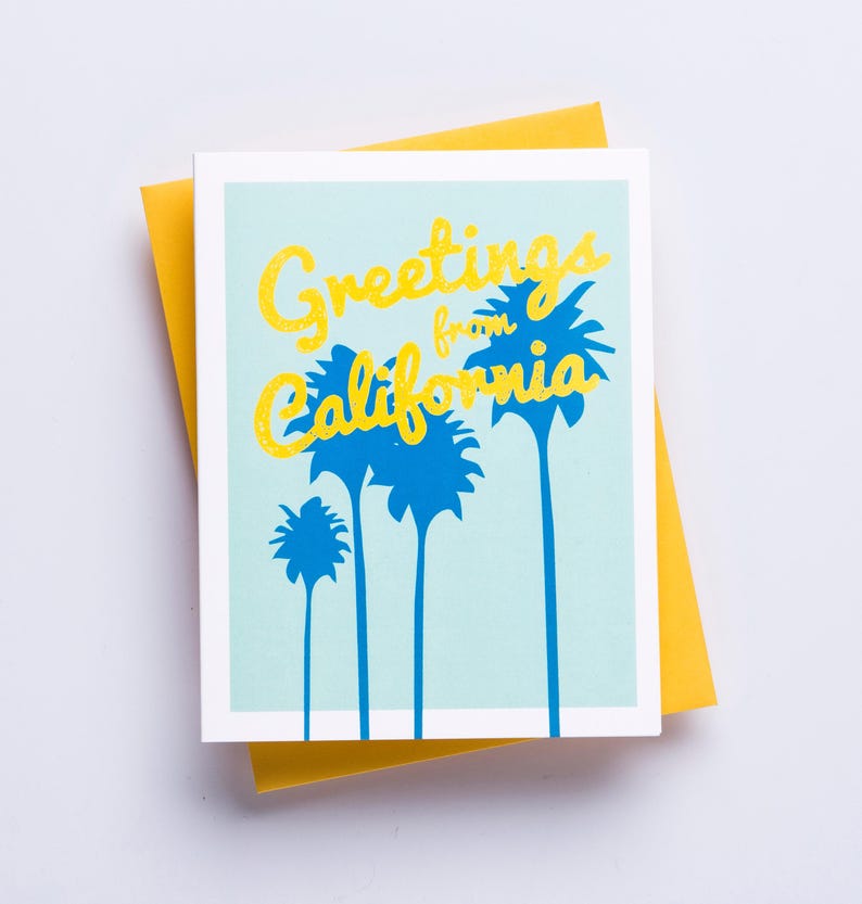 May include: A greeting card with a blue sky background and yellow text that reads "Greetings from California". The text is surrounded by blue palm trees.