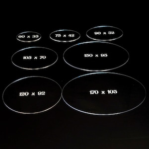 May include: Seven clear acrylic oval bases of varying sizes, each with white text indicating dimensions in millimeters. The largest base measures 170 x 105 mm, while the smallest is 60 x 35 mm. All are set against a black background.