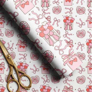 May include: A roll of white wrapping paper featuring a repeating pattern of pink and red gift boxes, heart-shaped balloons, and bows, accompanied by a pair of gold-toned metal scissors with ornate handles resting on the paper surface.