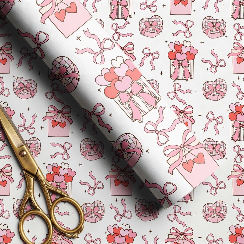 May include: A roll of white wrapping paper featuring a repeating pattern of pink and red gift boxes, heart-shaped balloons, and bows, accompanied by a pair of gold-toned metal scissors with ornate handles resting on the paper surface.