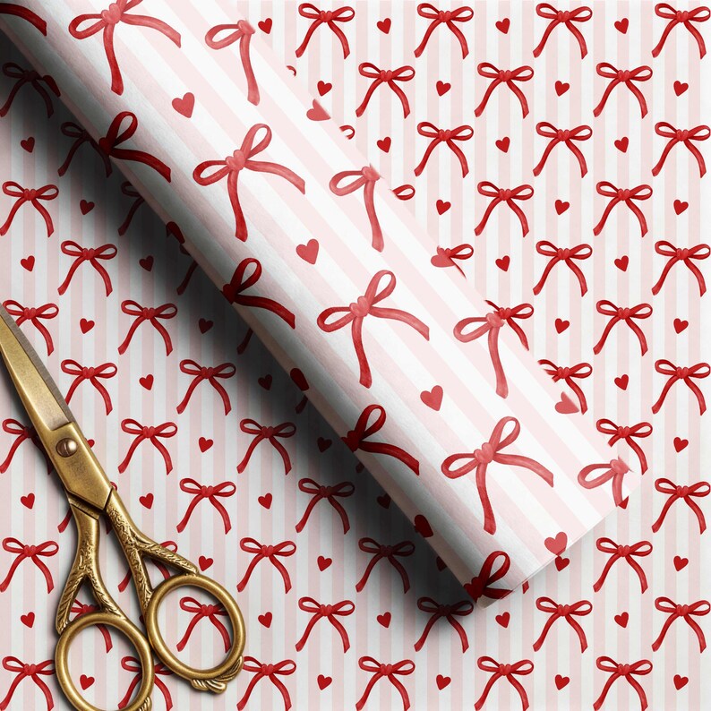 May include: A roll of wrapping paper featuring a repeating pattern of red bows and small red hearts on a background of vertical white and light pink stripes, positioned next to a pair of ornate gold-colored metal scissors with intricate handle details.