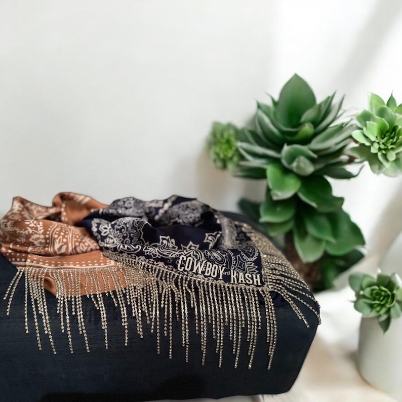 May include: A black and brown paisley bandana with a gold fringe and the text "COWBOY CASH" embroidered on it.