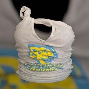 May include: White t-shirt with a blue and yellow jaguar logo and the words "SOUTHERN JAGUARS" printed across the front. The shirt is knotted at the top, creating a unique design. The shirt is made of a soft, lightweight material.