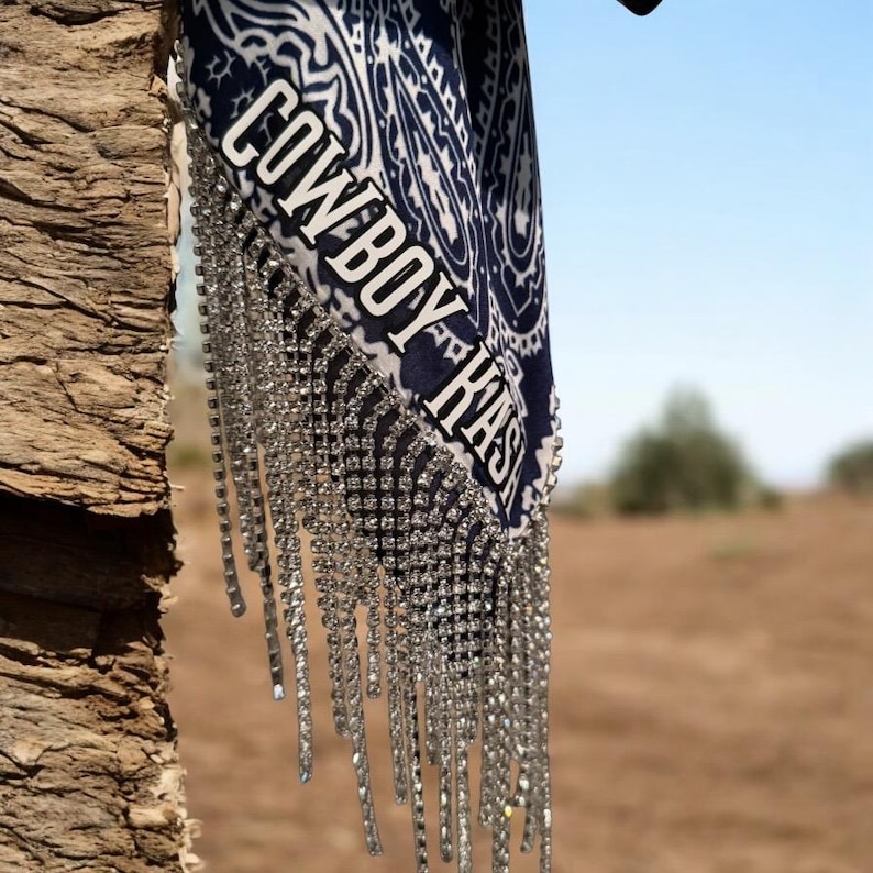 May include: A blue and white paisley bandana with the text "COWBOY HASH" in white lettering. The bandana has a fringe of silver rhinestones.