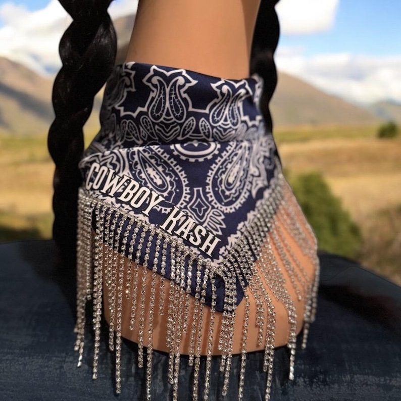 May include: A blue bandana with a paisley pattern and the text "COWBOY HASH" in white. The bandana has a fringe of silver rhinestones.
