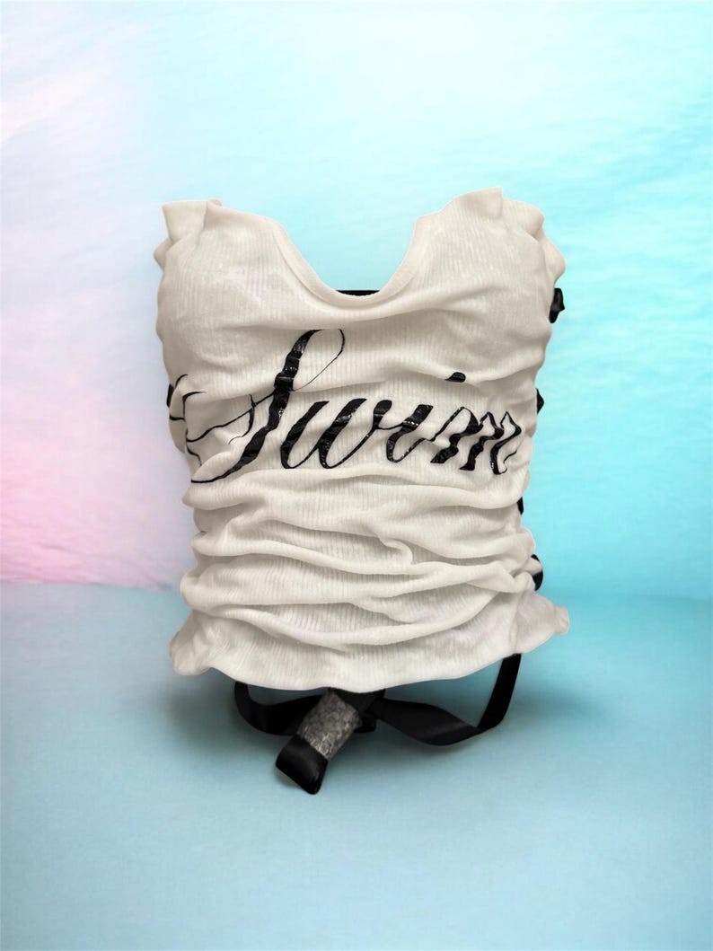 May include: White ruched top with the word "Summer" in black script. The top has a scoop neck and a black ribbon detail at the bottom. The background is a gradient of blue and pink.