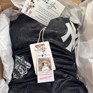 May include: A black mesh baseball jersey and shorts set with white accents, featuring the New York Yankees logo. The set is packaged in a box with a thank you card and a Mitchell & Ness tag.