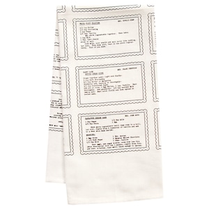 May include: White tea towel with brown text featuring vintage recipes for White Frosting, Party Cake (Butter Cream Icing), and Radiation Remove Cake. The recipes are printed in a vintage font style.