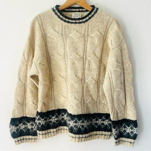 May include: Cream-colored cable knit sweater with a navy blue and white patterned band at the hem and cuffs. The sweater has a crew neck with navy blue stripes. The brand "LOFT" is visible on the label.