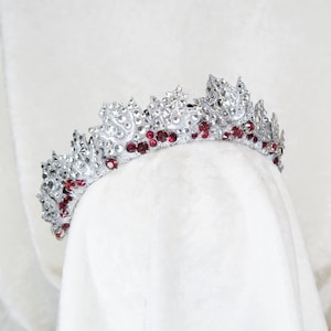 Op de afbeelding: Een zilveren kroon met rode strass-accenten. De kroon is gemaakt van metaal en heeft een delicaat ontwerp.