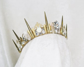Op de afbeelding: Een gouden kroon met spikes en heldere kristallen. De kroon is versierd met witte stenen en heeft een delicaat ontwerp.