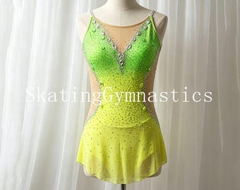 May include: A lime green and yellow ombre leotard featuring a sheer nude mesh neckline and side panels, adorned with numerous clear crystals and larger decorative stones. The garment includes a short skirt and the text SkatingGymnastics.