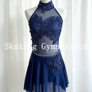 May include: A navy blue sleeveless dress with a high neck, sheer mesh panels, and intricate dark blue lace appliqués adorned with beads and sequins. The skirt features a layered chiffon design, and the text Skating Gymnastics is visible.