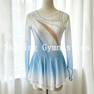 May include: A long-sleeved skating dress featuring an ombre gradient from white at the top to light blue at the bottom. The bodice is adorned with clear crystals and includes a sheer mesh panel. The skirt has a layered hemline with light blue trim.
