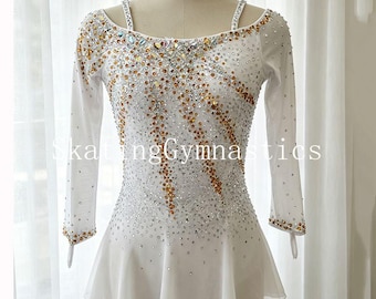 Può includere: Un body bianco a maniche lunghe con scollo rotondo, spalline sottili e gonna svasata. Il corpetto è decorato con un fitto motivo di cristalli trasparenti e color ambra disposti in linee diagonali. Il testo SkatingGymnastics è visibile.