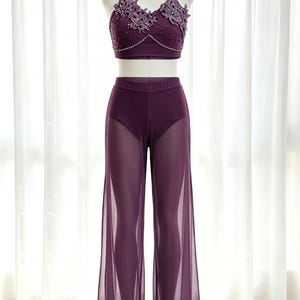 May include: A deep purple two-piece outfit consisting of a cropped top and wide-leg trousers. The top features intricate floral lace appliqués, beadwork, and thin straps. The trousers have an opaque high-waisted base with sheer, flowing outer panels.
