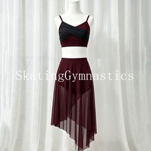 May include: A two-piece dance outfit featuring a burgundy and black crisscross crop top with thin straps and a matching burgundy high-waisted skirt with an asymmetrical sheer mesh overlay. The text SkatingGymnastics is visible across the center.