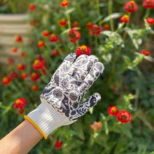 Op de afbeelding: Een witte tuinhandschoen met een zwarte botanische print en vogelmotieven. De handschoen heeft een geribbelde witte boord met een dunne gele rand, ontworpen voor handbescherming tijdens het werken met planten en bloemen in de tuin.