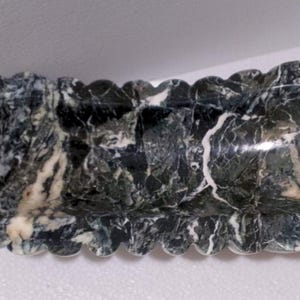 May include: A long, oval-shaped marble dish with a scalloped edge. The dish is made of green and white marble with a swirling pattern.