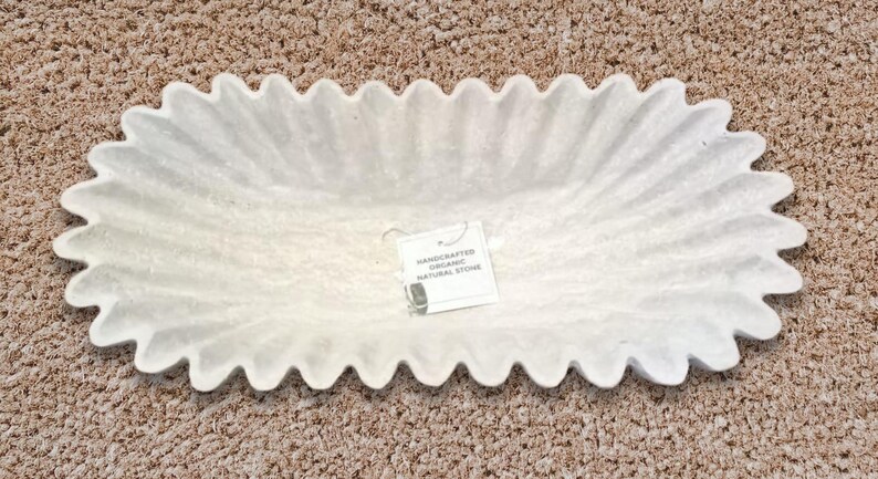 May include: White oval-shaped serving dish made of natural stone with a scalloped edge. The dish has a handmade organic look. The label reads "Handcrafted Organic Natural Stone".