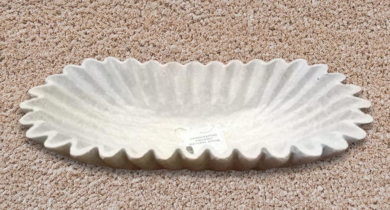 May include: A white oval-shaped ceramic planter with a fluted edge. The planter has a textured surface and a label on the bottom.