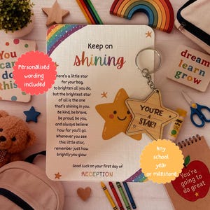 Op de afbeelding: Een houten stervormige sleutelhanger met de gegraveerde tekst 'YOU'RE A STAR!' bevestigd aan een displaykaart met een regenboog, een getekende ster en een gedicht dat begint met 'Keep on shining' en eindigt met 'Good Luck on your first day of RECEPTION'.