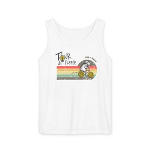 May include: White tank top with a distressed graphic. The graphic features a sheep riding a bicycle with yarn wheels, set against a striped background. Text reads "Tour de Fleece" and "July 2026".