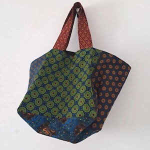 Może przedstawiać: Duża torba typu tote wykonana z tkaniny z patchworkowym wzorem. Torba ma wzór w kolorze niebieskim, zielonym i pomarańczowym z czerwono-pomarańczowym uchwytem.