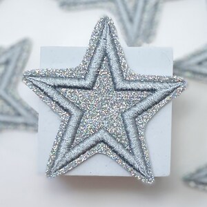 May include: A silver glitter star-shaped patch with a double-stitched outline.