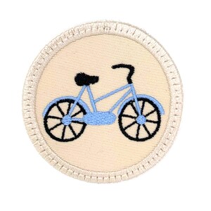 May include: A light blue bicycle embroidered on a beige circular patch with a white border.