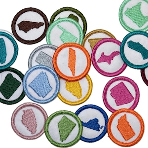 May include: A collection of embroidered patches featuring state outlines in various colors. Each patch has a white center with a state shape, surrounded by a colored border and a white outer ring. The patches are circular and appear to be made of fabric.