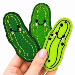 May include: Three embroidered fabric patches shaped like pickles. Two patches are a deep forest green with lighter green stitching details, and one patch is a bright lime green with black embroidered outlines and small black circular accents.