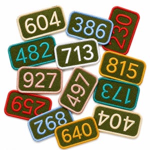 May include: A collection of rectangular olive green embroidered patches, each featuring a three-digit number stitched in various colors including white, light blue, red, yellow, pink, and teal, with matching colored borders around each patch.