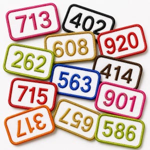 May include: A collection of rectangular embroidered patches with white centers and colored borders. Each patch features a three-digit number in a matching thread color, including 713, 402, 920, 262, 608, 414, 563, 715, 901, 317, 657, and 586.