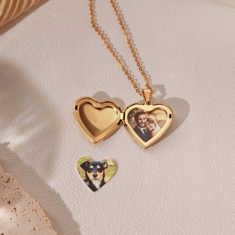 May include: Gold heart-shaped locket necklace with a photo of a couple inside. The locket is open and a separate photo of a dog is visible on the table.