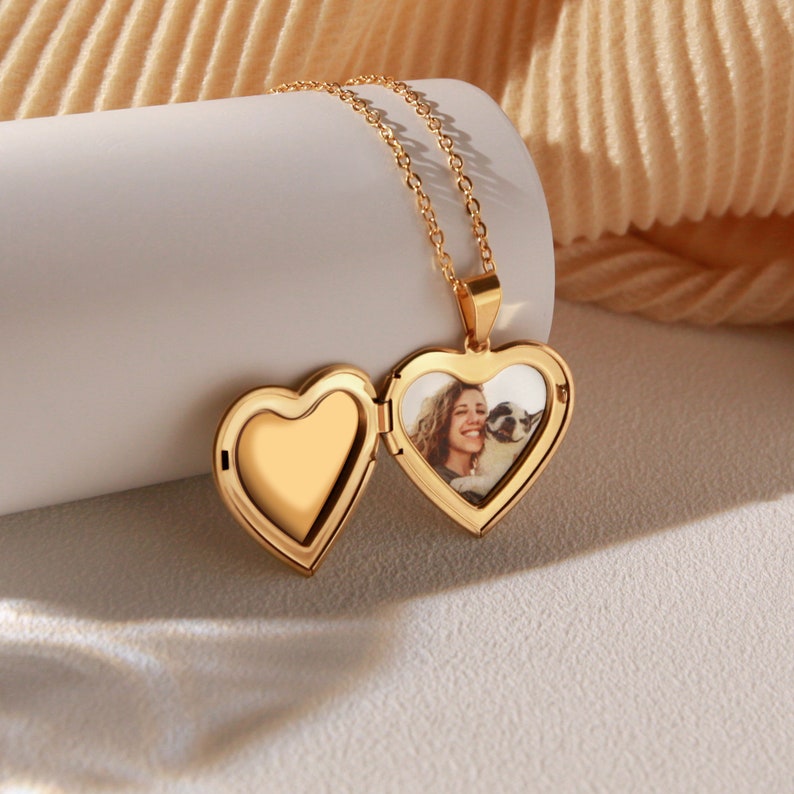May include: A gold heart-shaped locket necklace with a photo of a woman and a dog inside. The locket is open and the chain is visible.