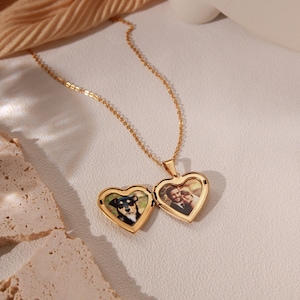 May include: A gold heart-shaped locket necklace with two photos inside. One photo shows a couple, and the other shows a dog.