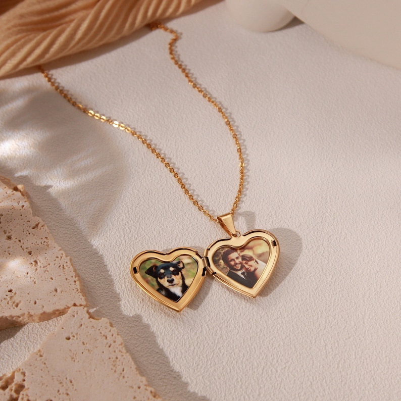 May include: A gold heart-shaped locket necklace with two photos inside. One photo shows a couple, and the other shows a dog.