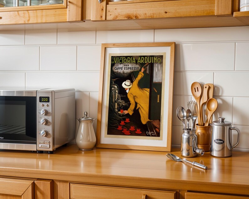 Puede incluir: Un p&oacute;ster vintage enmarcado de Victoria Arduino Caffe Espresso. La obra de arte presenta a un hombre con un abrigo amarillo sirviendo caf&eacute; espresso. La imagen est&aacute; sobre una encimera de madera con un microondas, utensilios y una jarra de metal.